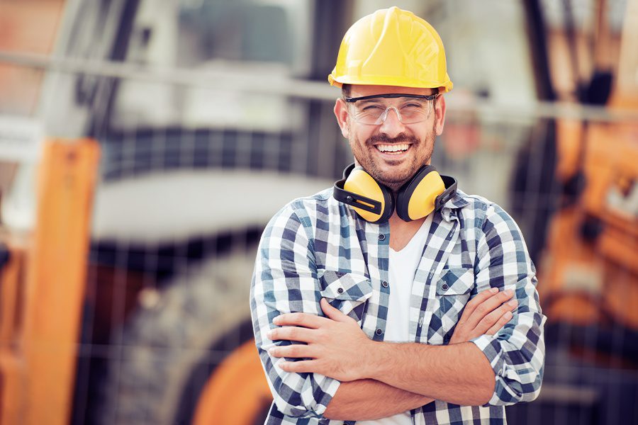 Business Insurance - Smiling Construction Worker at Site with Equipment Blurred in the Background