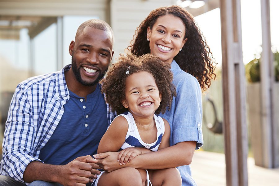 Life Insurance - Happy Family Portrait Sitting Outside of Home on a Sunny Day